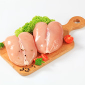 two pieces of raw chicken breast on the wooden cutting board decorated with a leave of green parsley, lettuce, pepper and red cherry tomatoes